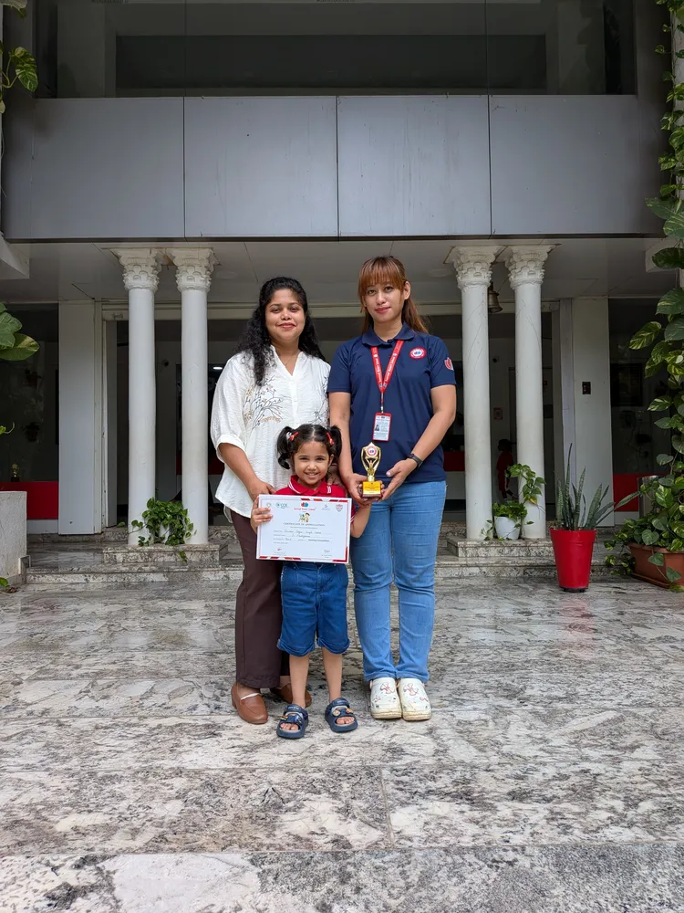 A Drawing Competition winner holding a certificate and trophy with two teachers