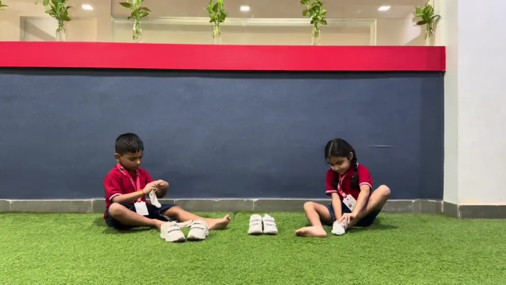 Two children sitting on the grass practising dressing themselves