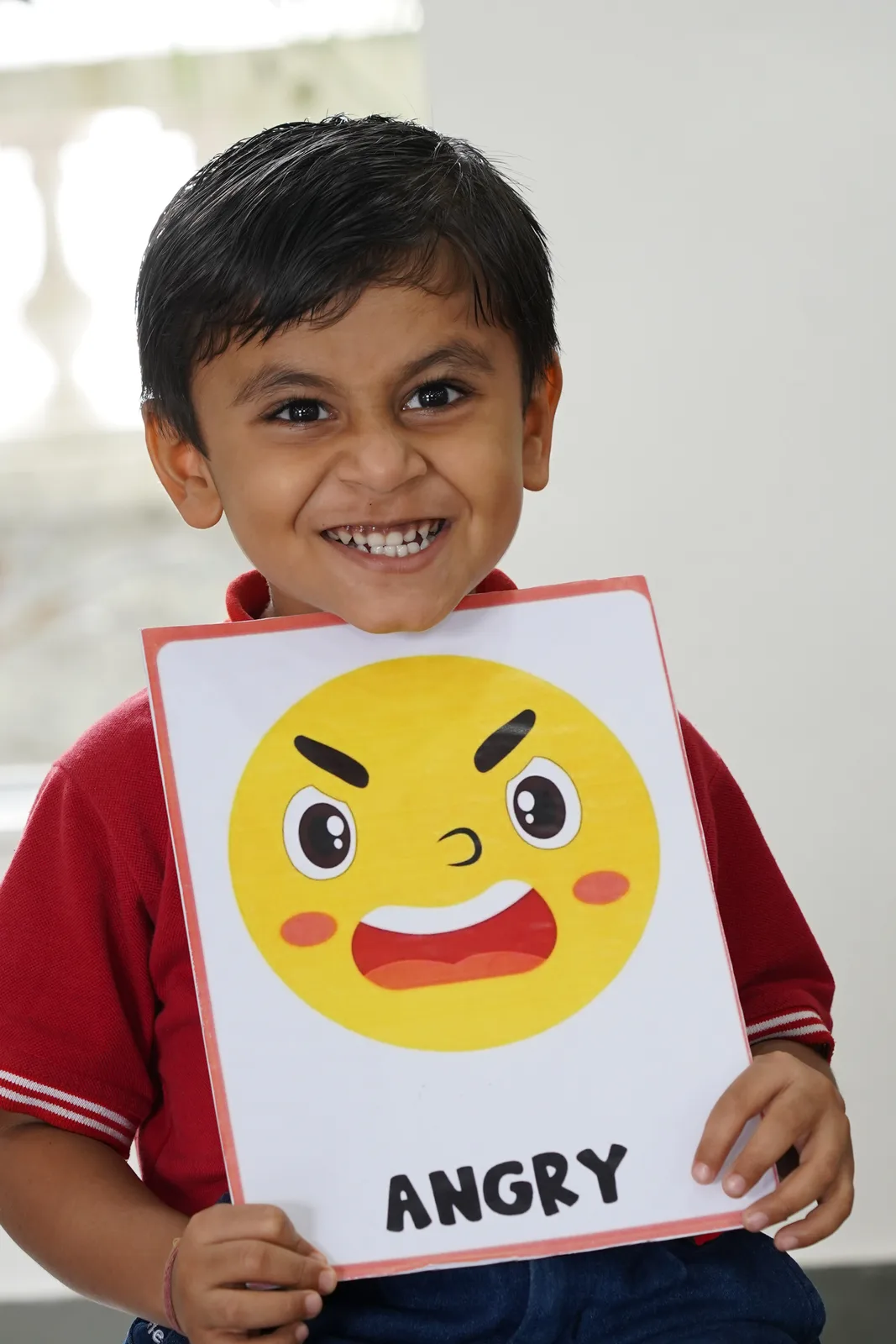 A Pre-Primary child holding an 'Angry' emotion flashcard
