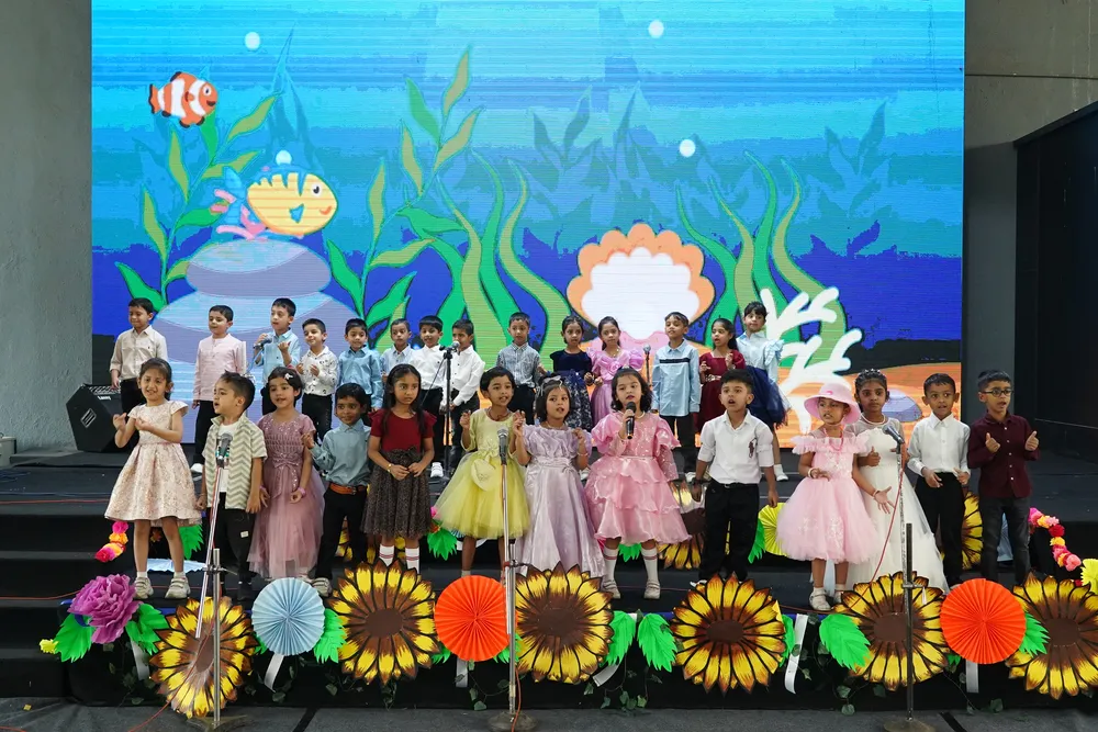 Children in pastel outfits on stage against an underwater backdrop