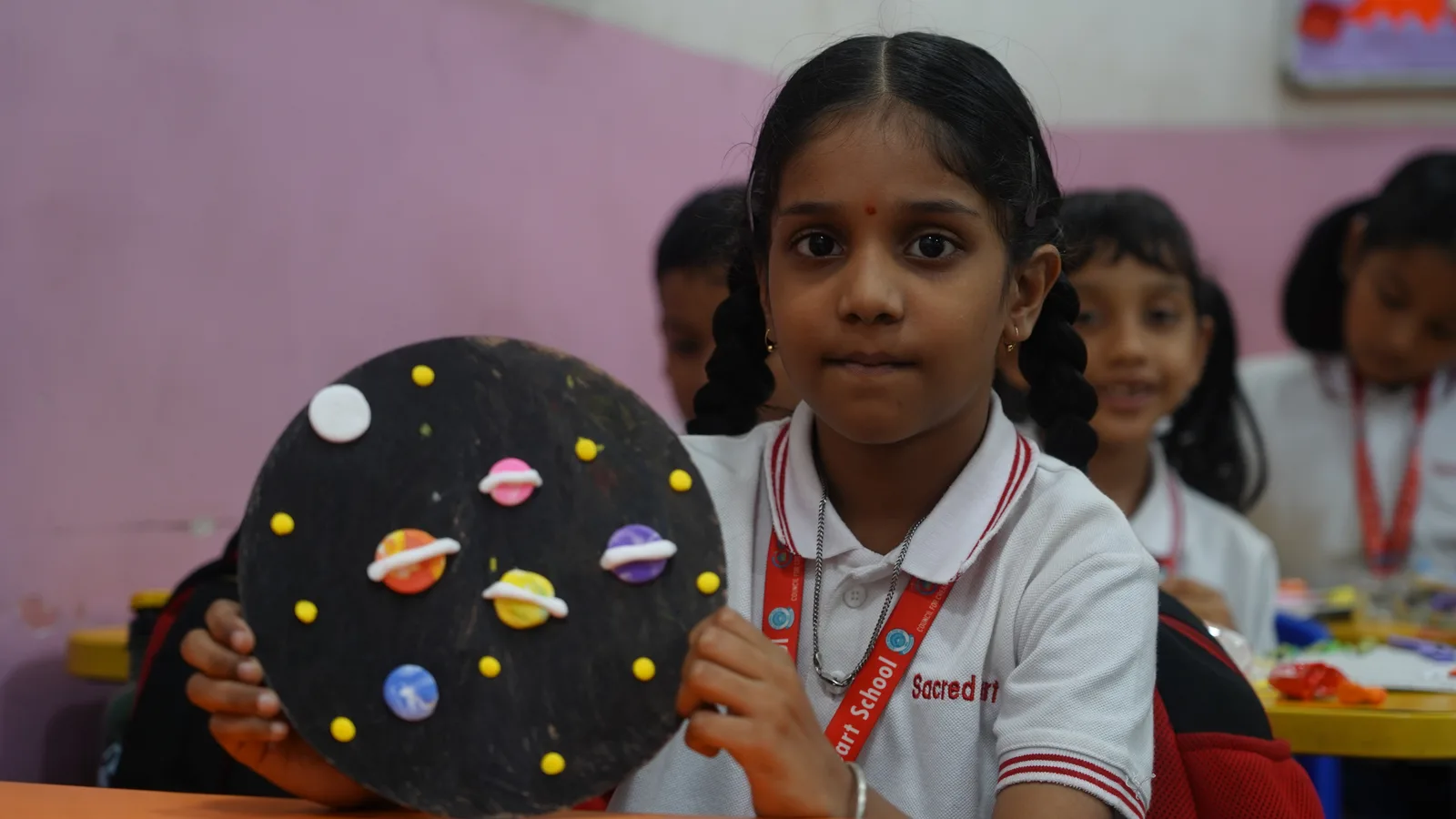 A Primary student holding a clay model of the solar system