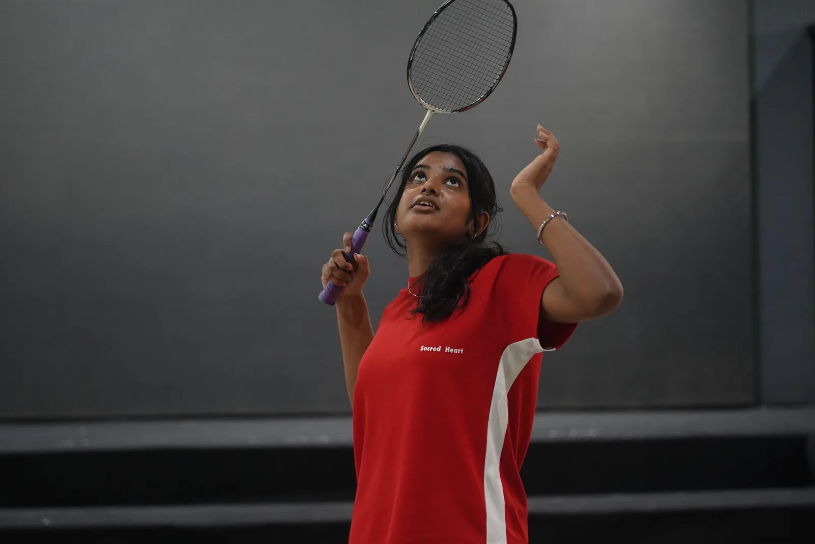A student serving during a badminton match indoors